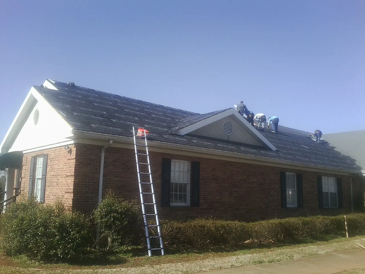 Crew tearing shingles off a brick ranch roof with a ladder set — Metal Roof Repair work by our crew in South Burlington