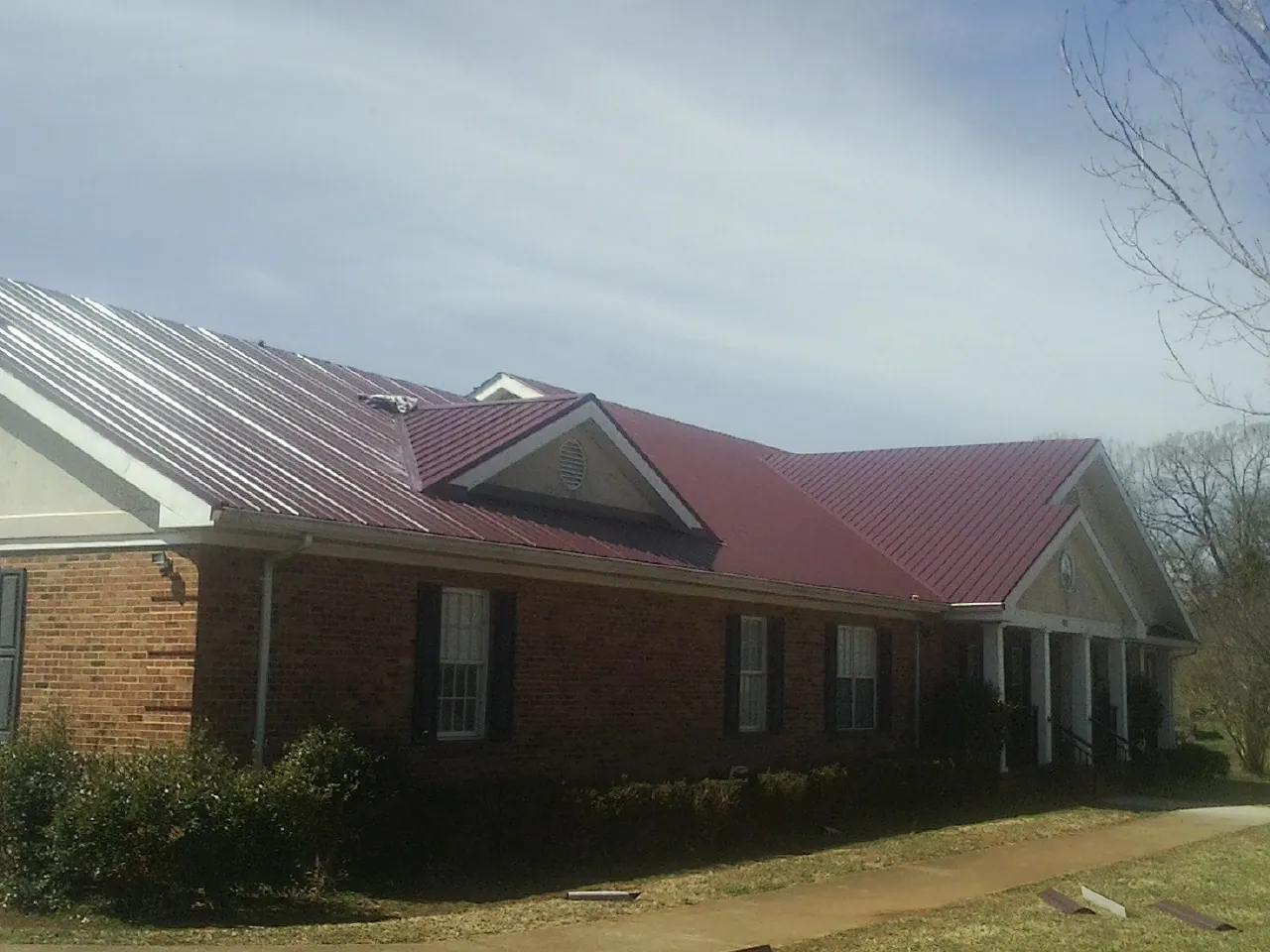 Red metal roof with gabled entries on a long brick building, from a Hail Damage Roof Repair job in South Burlington