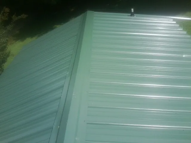 New green metal panels meeting at the ridge of a roof — Flat Roof Repair work by our crew in South Burlington