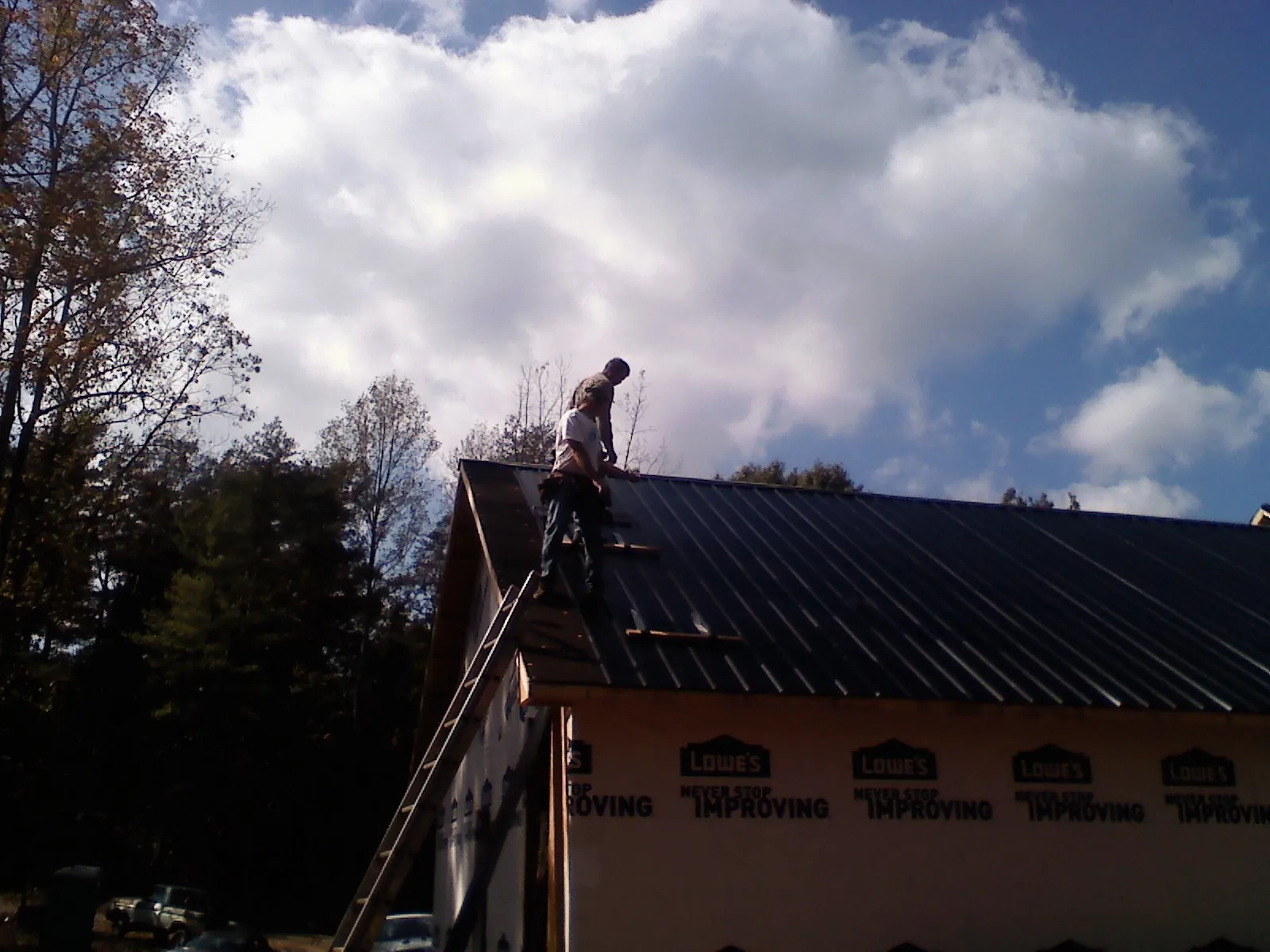 Roofer fastening dark metal panels high against a cloudy sky, from a Roof Inspection job in South Burlington