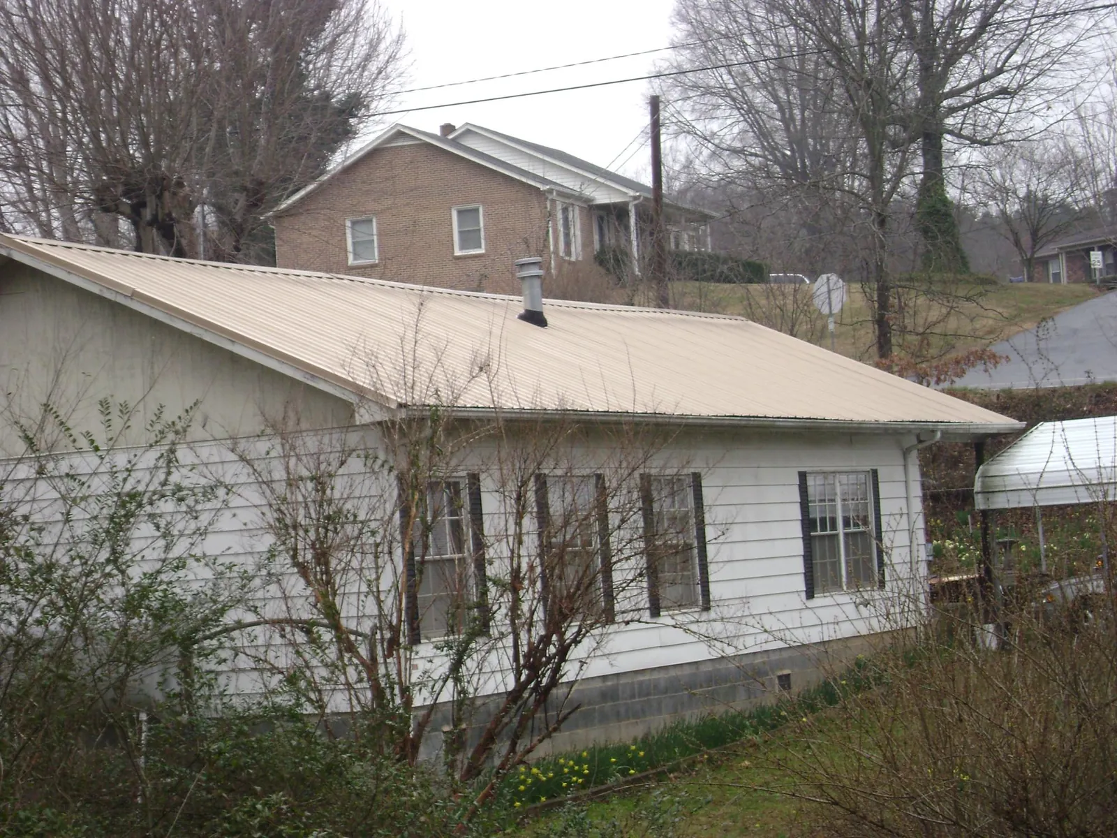 Tan metal roof on a white sided house set into a hillside — Commercial Roofing by Roofing Brothers in South Burlington